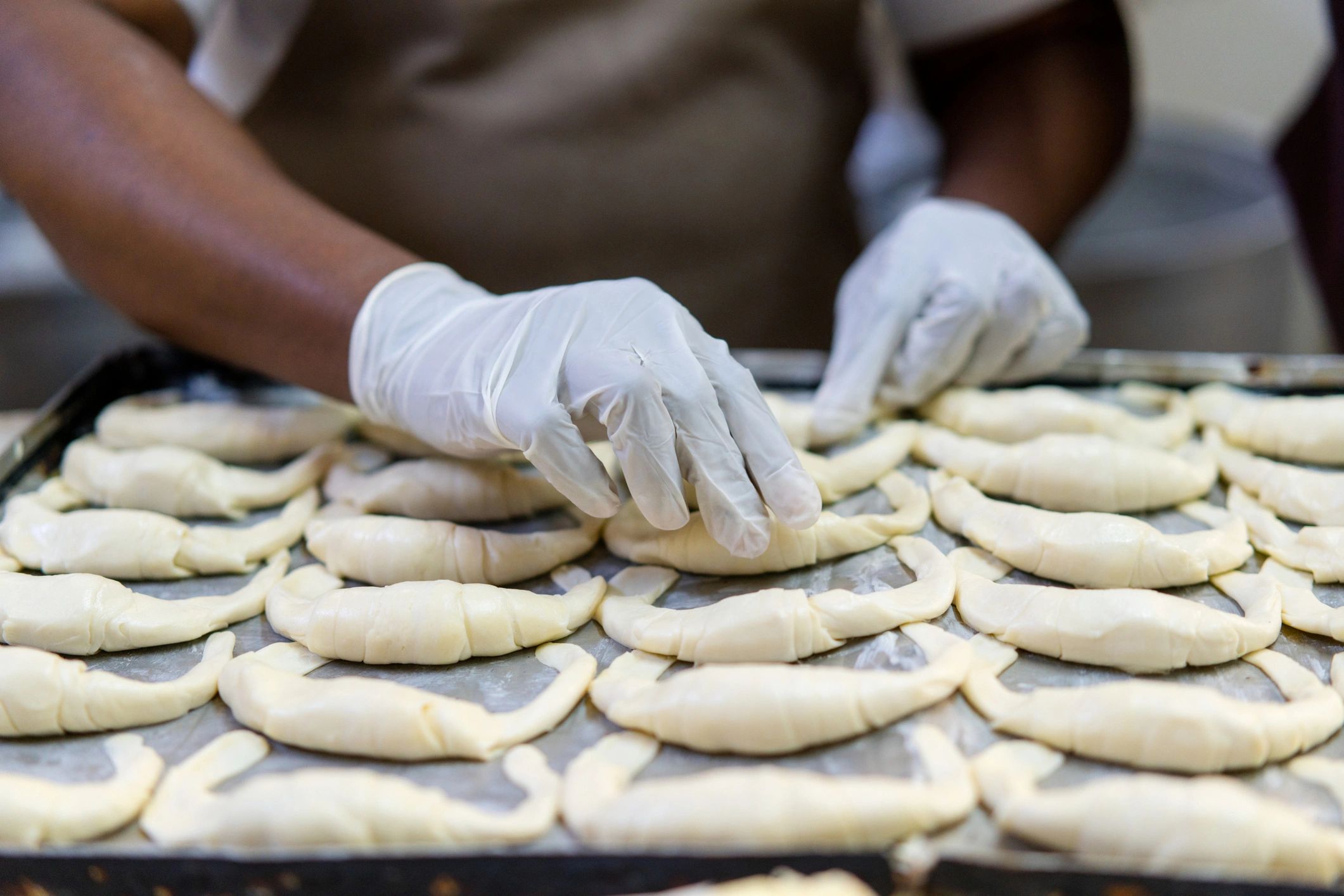 Baker shaping croissants on a tray in a warm bakery kitchen